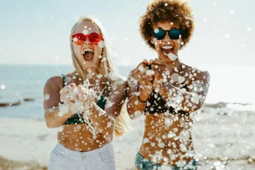 Zwei Freundinnen lachen am Strand und spritzen mit Wasser