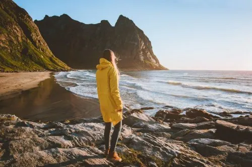 Frau in gelber Regenjacke blickt auf Strand und Berge