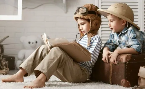 Zwei Kinder mit Pilotenmütze und Tropenhelm lesen gemeinsam in einem Buch