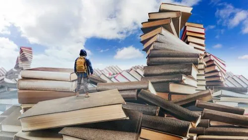 Wanderer mit Rucksack klettert über riesige Bücherstapel vor blauem Himmel
